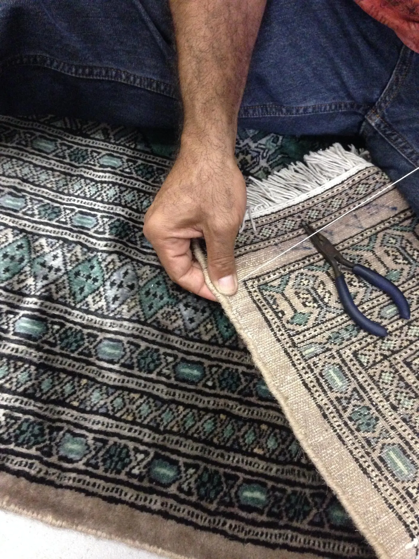 Manos de un especialista reparando el borde de un tapete con hilo y pinzas